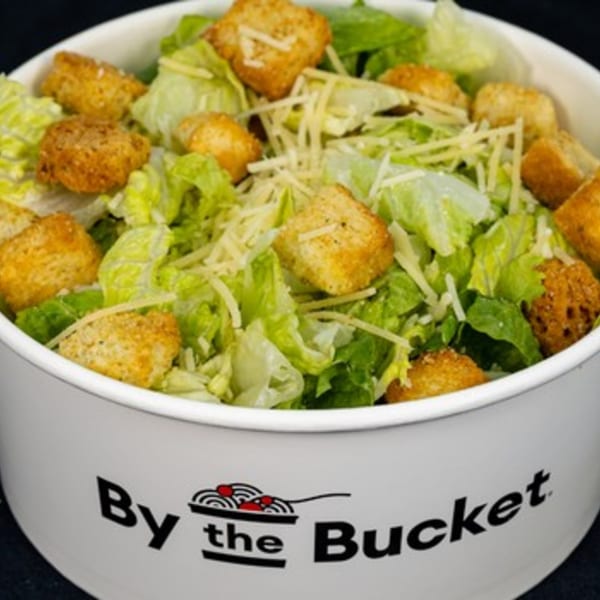 Caesar salad with croutons and shredded cheese in a white By the Bucket branded container.
